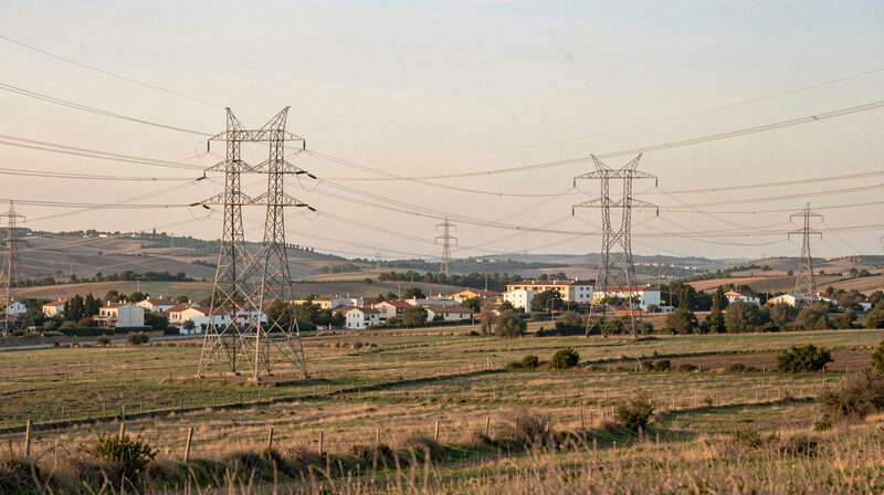Torres de alta tensión y líneas eléctricas cruzando el campo abierto junto a un pueblo español al final de la tarde